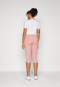 Hvit polo skjorte med rosa krage, kombinert med lyse rosa cropped bukser med splitt i nederkant. Brukt med hvite joggesko.
