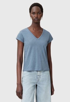 V-neck short-sleeve T-shirt in soft blue fabric, featuring a relaxed fit and rolled cuff details, paired with light-wash wide-leg jeans.