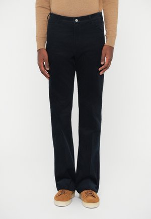 Tmavomodré kordové nohavice so strihom do rovna, so klasickým gombíkom na páse, prednými vreckami a jemnou textúrou. Nosené s hnedými teniskami.