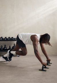 Poignées de pompes avec des poignées noires et des accents jaunes sur un sol lisse et gris clair. Haltères et kettlebells en arrière-plan.