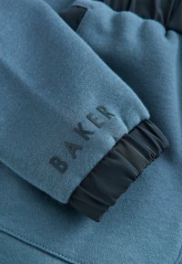 Blauwe sweatshirt manchette met een geribbelde zwarte elastische band en een reliëf "BAKER" logo. Het materiaal heeft een soepele textuur met een subtiele weving.