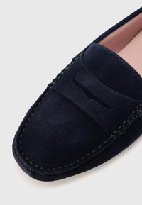 Tamsiai mėlyni zomšos loaferiai su apvalia nosimi, minimaliais siūlais ir dekoratyviniu plyšiu ant bato viršaus. Minkšta tekstūra, artimas vaizdas.