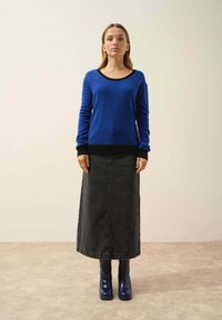 Modrý svetr s černými akcenty, doplněný černou džínovou midi sukní a modrými botami na podpatku. Hladká textura a ležérní design.