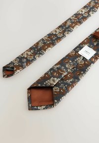Brun og marineblå blomsteret mønstrede slips lavet af polyester; har en glat tekstur og en kontrasterende ensfarvet brun inderside. Inkluderer et mærke med branding.