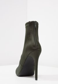 Gröna satäng ankelboots med hög stilettklack, med sidodragkedja och slät yta, designade för en figurnära silhuett.