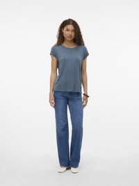 Teal t-skjorte med kort erme og rund hals, kombinert med blå vide jeans og lyse sko. Glatt stoff, komfortabel passform.