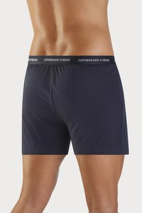 Mørkeblå bomullboxershorts med myk elastisk midje og "COPENHAGEN STUDIOS" trykt i hvitt, minimalistisk design.