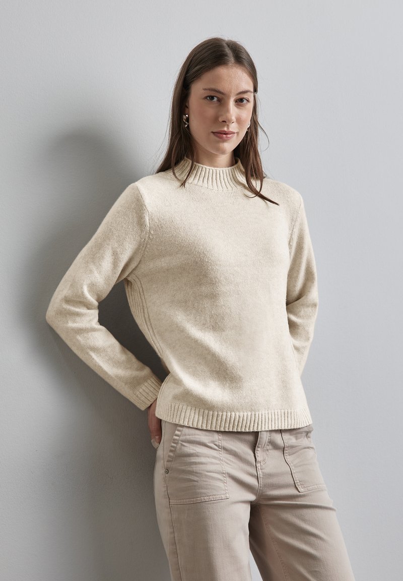 Pull en tricot couleur crème avec un col haut côtelé, des manches longues et une coupe décontractée. Tissu doux texturé avec un ourlet et des poignets côtelés.