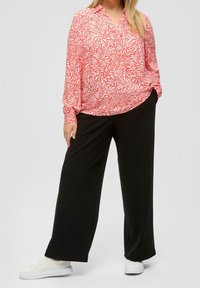 Bluzka w kwiatowy wzór w kolorze koralowym i bia�łym, z długimi rękawami, połączona z czarnymi spodniami o wysokim stanie i szerokimi nogawkami oraz białymi trampkami.