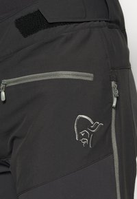 Pantalons d'extérieur noirs avec poches zippées grises, tissu texturé et détail de logo brodé. Présente un système de fermeture à scratch à la taille.