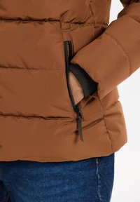 Brun pufferjakke med en lynlåslomme, elastiske manchetter og en quiltet tekstur. Stoffet har en glat overflade og en let glans.