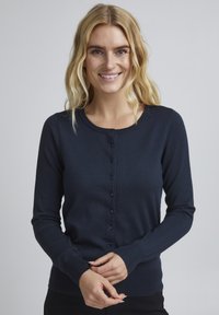 Mörkblå stickad cardigan med långa ärmar, rund halsringning och knäppning fram. Har ribbade muddar och nederkant. Slät textur.