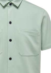 Hellgrünes Kurzarmhemd mit Kragen, aus strukturiertem Stoff, zwei Brusttaschen und schwarzen Knöpfen.