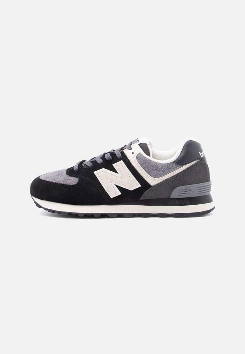 Chaussure de course New Balance pour homme avec une tige en suède et mesh noire, grise et blanche, logo blanc et semelle amortissante sur un fond clair.