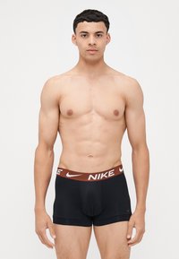 Črne moške bokserice z rjavim pasom, na katerem je belo "NIKE" blagovno ime. Material se zdi gladek in oprijemajoč.