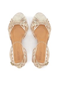 Zelta krāsas plakanas sandales ar siksniņām un pinuma detaļu pār pirkstiem, kā arī potīšu sprādzēm, bēšas zolītes, iekšpusē drukāts zīmola nosaukums "kazar".