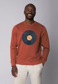 Rustkleurige sweatshirt met een ronde grafische afbeelding van een vinylplaat in blauw en beige, met een textuurafwerking en ribbels aan de mouwen.