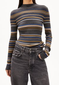 Pull rayé côtelé dans des tons de gris, marron et bleu. Design ajusté avec col montant et manches longues, associé à un jean taille haute gris foncé.