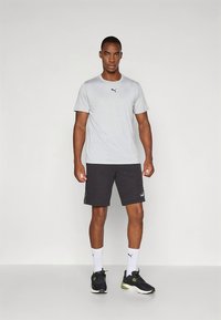 Grå kortermet skjorte med en liten svart logo, kombinert med svarte treningsshorts, hvite sokker og svarte joggesko med grønne detaljer.