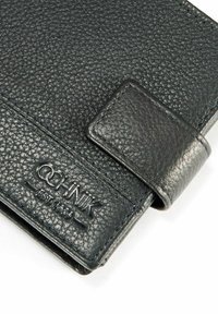 Czarny portfel z teksturowanej skóry, z gładkim klapą i przeszyciami; na przodzie ma wyembossowane logo „OCHNIK EST 1989”.