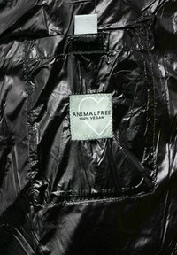 Tejido negro y brillante con una etiqueta verde prominente que dice "ANIMALFREE 100% VEGANO". Presenta un pequeño bolsillo cosido en el interior.