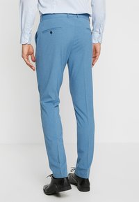 Pantalones de hombre en un suave tono azul claro, confeccionados con un tejido de textura lisa. Cuentan con bolsillos inclinados, bolsillos traseros con botón y un corte ajustado.