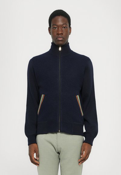 Pull à zip marine avec col montant, orné d'accents multicolores sur les poches avant, avec des poignets et un ourlet côtelés, texture douce.