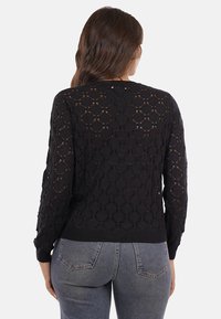 Maglione nero lavorato a maglia con un intricato motivo a rombi, maniche lunghe e scollo rotondo. Testurizzato con polsini e orlo a coste.