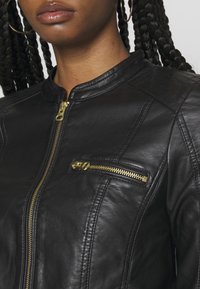 Czarna skórzana kurtka motocyklowa z zamkiem błyskawicznym, wyposażona w małą kieszeń na zamek i pikowane detale na ramionach. Widoczne złote elementy ozdobne.