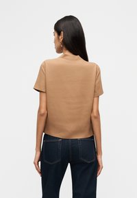 Καφέ τοπ με κοντά μανίκια και ελαφρώς κομμένη σχεδίαση, με λεία υφή και διακριτικό γιακά, συνδυασμένο με σκούρο τζιν.