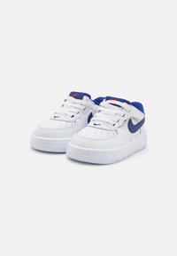 White leather sneakers with blue accents, featuring a perforated toe, lace-up closure, and textured rubber sole. Nike branding visible.