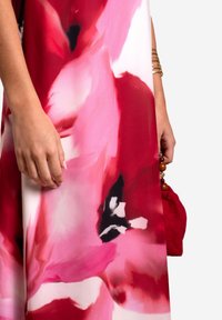 Maxikleid in lebhaftem roten und pinken Blumenmuster, aus weichem Stoff, mit lockerer Passform und einem Accessoire, einer kleinen roten Handtasche mit Holzperlen.