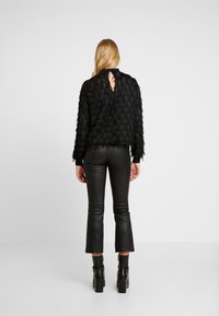 Top nero e testurizzato con un design a frange stratificate. Presenta una scollatura a chiave sul retro, abbinato a pantaloni in pelle nera aderenti e stivali con tacco.