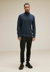 Mörkblå polotröja i en strukturerad stickning, matchad med svarta byxor med uppvikta ben och kraftiga svarta stövlar, stående på en neutral bakgrund.