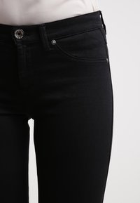 Černé denimové džíny s úzkým střihem, pěti kapsemi a kovovým zapínáním. Hladká textura s jemným prošíváním.