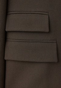 Gros plan sur deux poches à rabat en tissu à petits carreaux marron et noir, probablement une partie d'un manteau ou d'une veste.