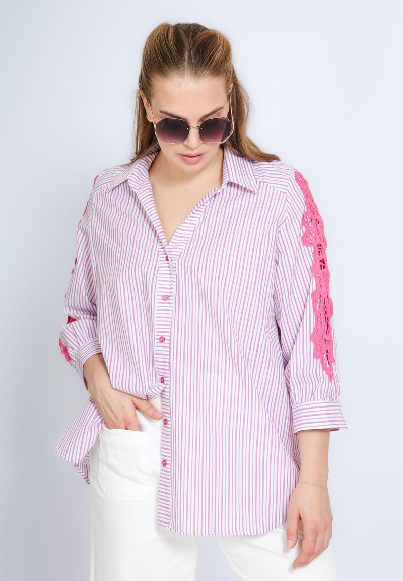 Gestreepte blouse in lichtroze en wit met kantaccenten op de mouwen, met een knoopsluiting aan de voorkant en een ontspannen pasvorm, gecombineerd met witte broek.