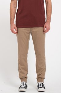 Pantalons beiges fuselés avec des poignets élastiques, en coton, poches latérales, portés avec des baskets noir et blanc, associés à une chemise bordeaux.