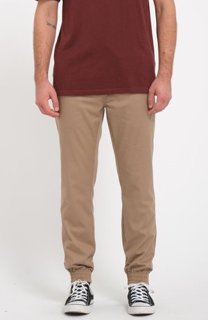 Beige taps met elastische boorden, van katoen, met zijzakken, gedragen met zwart-witte sneakers, gecombineerd met een bordeauxkleurig shirt.