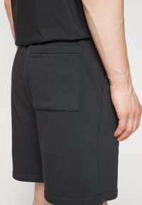 Svarta bomullsshorts med rak passform, en bakficka och en mjuk textur, med sömmar längs fållen och sidsömmarna.