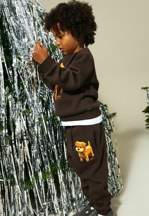 Brun genser og joggebukser med et pikselert design av en gul hund. Stoffet ser mykt ut; antrekket har en hvit midjebåndsdetalj.