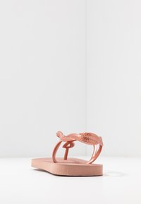 Chinelo de borracha rosa com uma alça texturizada que imita um padrão tecido, sola plana e bico arredondado. Design minimalista, sem adornos adicionais.