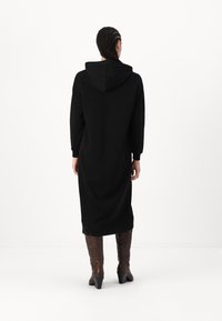 Μαύρο φόρεμα με κουκούλα και μακρυά μανίκια, μέχρι το γόνατο, φτιαγμένο από μαλακό ύφασμα. Συνδυασμένο με ψηλές καφέ μπότες με σχέδιο. Απλή, χαλαρή εφαρμογή.