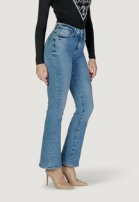 Jeans in denim azzurro chiaro a vita alta con fondo svasato, dotati di tasche frontali e passanti per cintura. Abbinati a tacchi alti color nude.