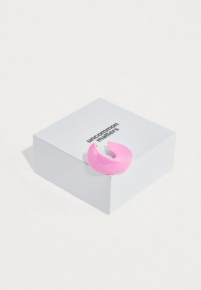 Ροζ δαχτυλίδι από ρητίνη με κυρτό, ανοιχτό σχέδιο, που ακουμπά σε ένα λευκό κουτί με την επιγραφή «uncommon matters». Ομαλή επιφάνεια.