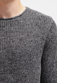 Graues und schwarzes gestricktes Sweatshirt mit einem strukturierten, gewebten Muster. Mit einem Rundhalsausschnitt und glattem Halsabschluss. Nahaufnahme des Stoffes.