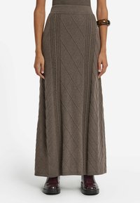 Lång brun stickad kjol med en texturerad diamantmönster, ribbad midja och en avslappnad passform. Bärs med glansiga burgundiska ankelstövlar.