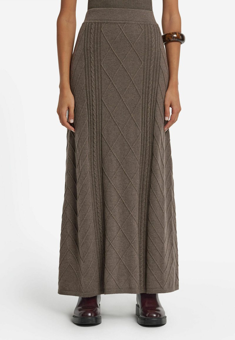 Lång brun stickad kjol med en texturerad diamantmönster, ribbad midja och en avslappnad passform. Bärs med glansiga burgundiska ankelstövlar.