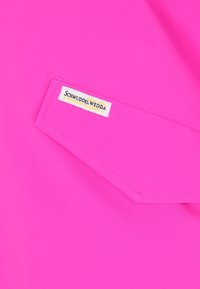 Material roz intens cu o clapetă de buzunar cusută, având o etichetă albă pe care scrie "Schmuddelwedda German Design Wenn Dat Pladdert."