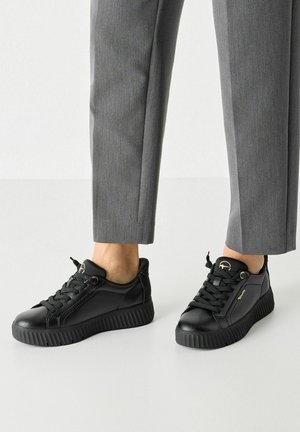 Baskets noires en cuir avec un design texturé, dotées de lacets ronds, d'une semelle striée et d'un petit logo en accent sur le côté.